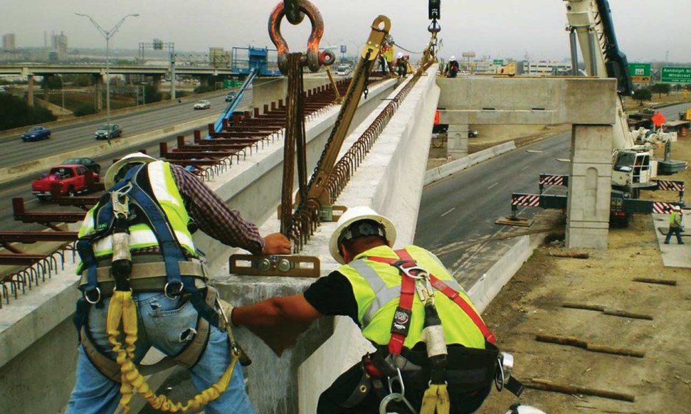 Workers rigging bridge girders over an active highway